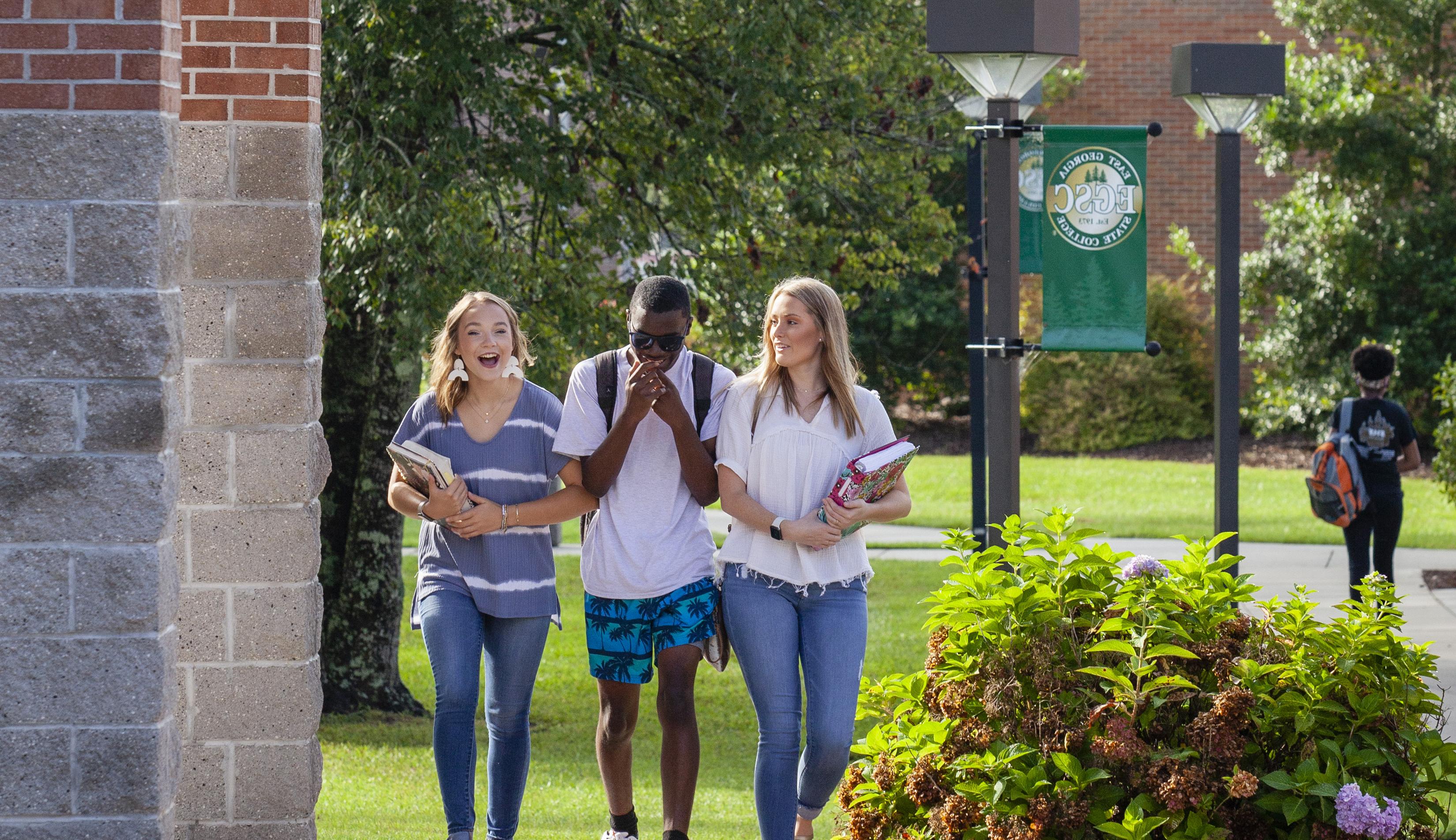 two female students and a male student laughing while walking through campus